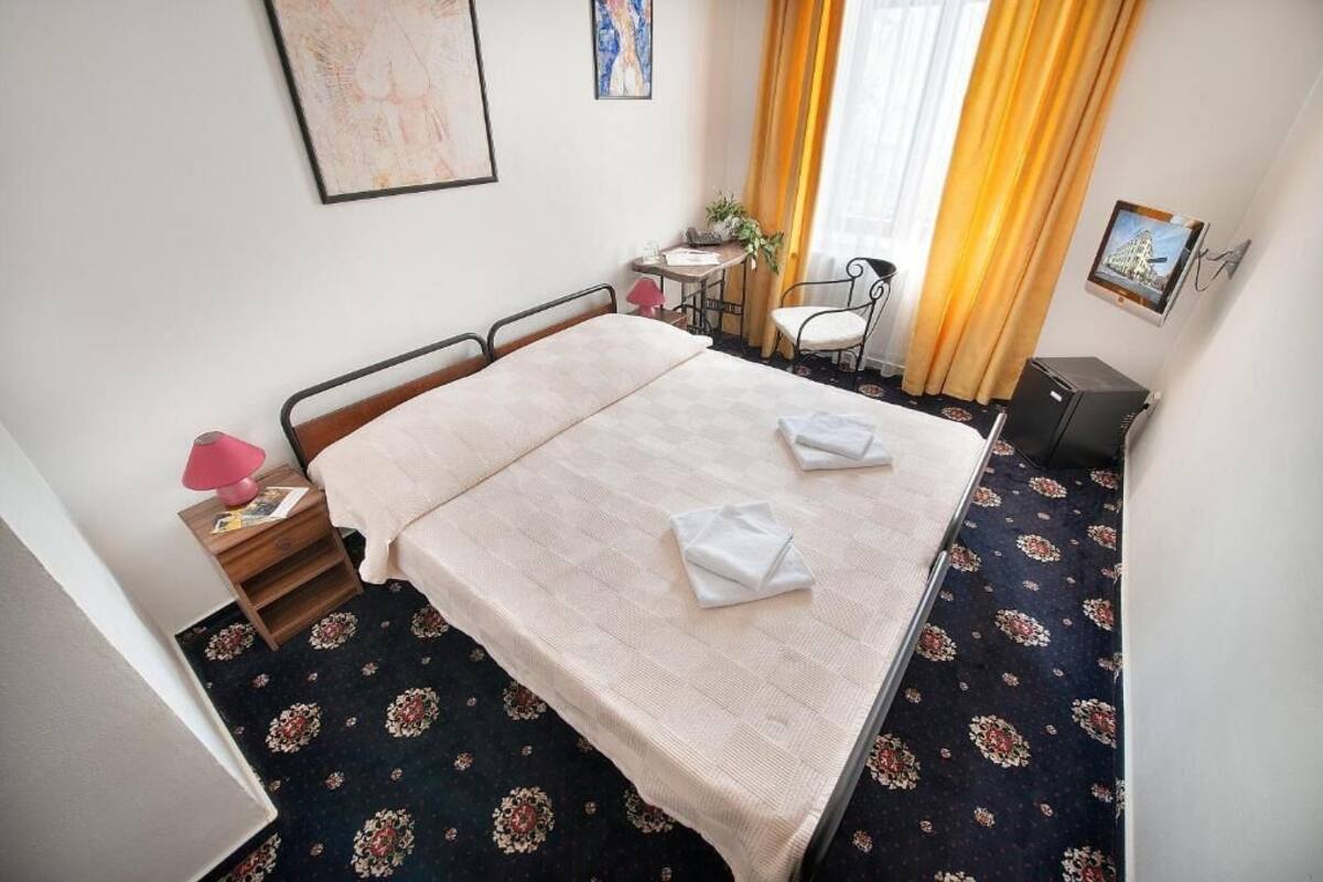 Une chambre d’hôtel avec un lit, une petite table avec une lampe, une chaise et un bureau avec un ordinateur.