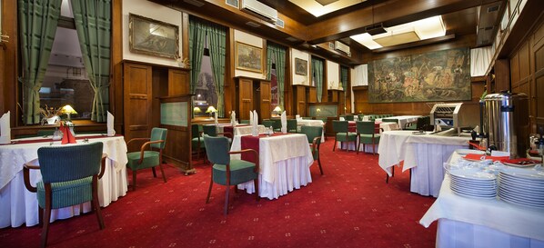 Un espace repas avec des tables dressées, des chaises à revêtement vert et un sol recouvert d’une moquette rouge.