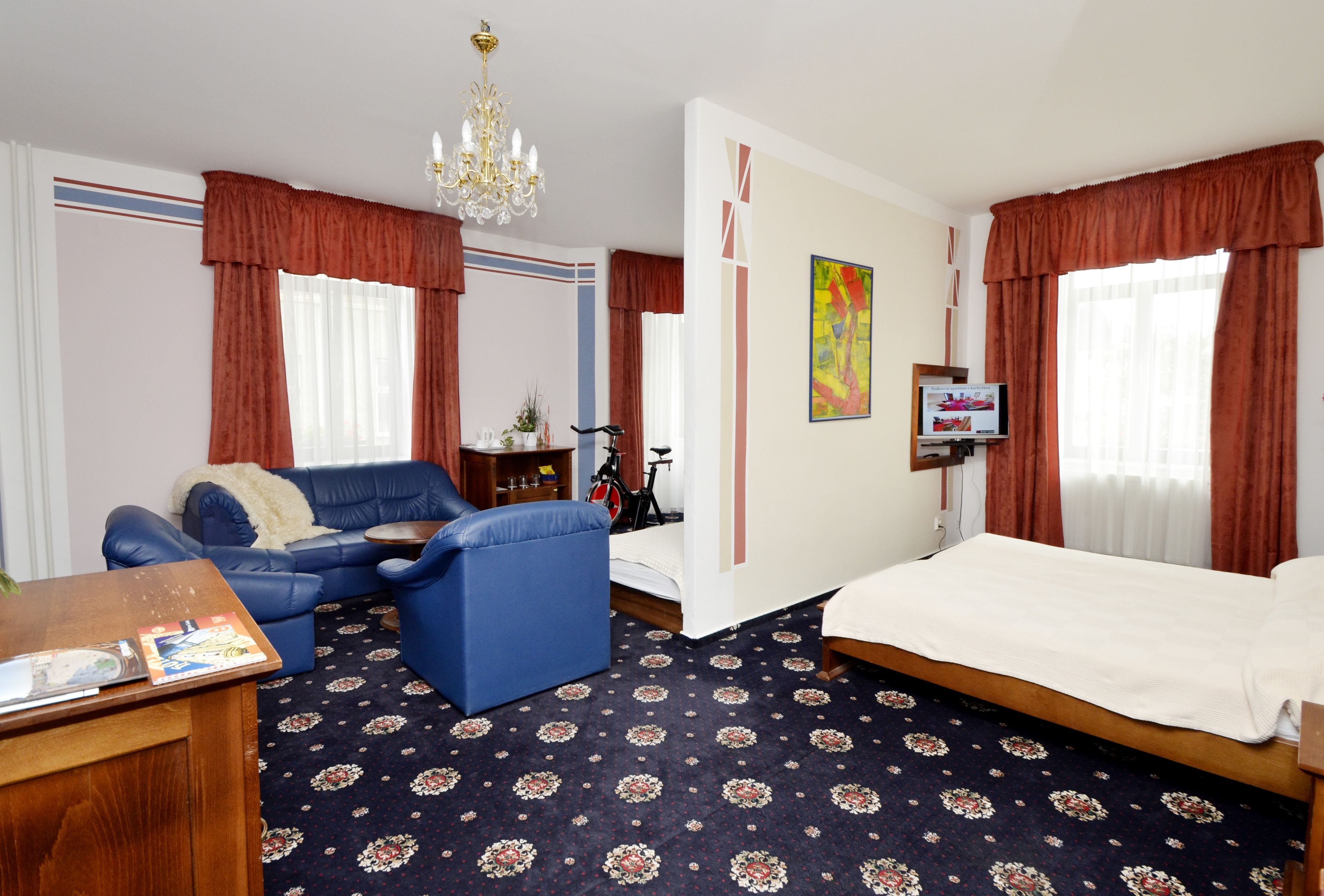 A hotel room with a bed, a blue sofa, a small table, a TV, and a chandelier.