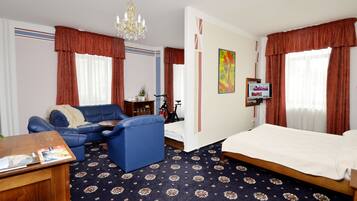 A hotel room with a bed, a blue sofa, a small table, a TV, and a chandelier.
