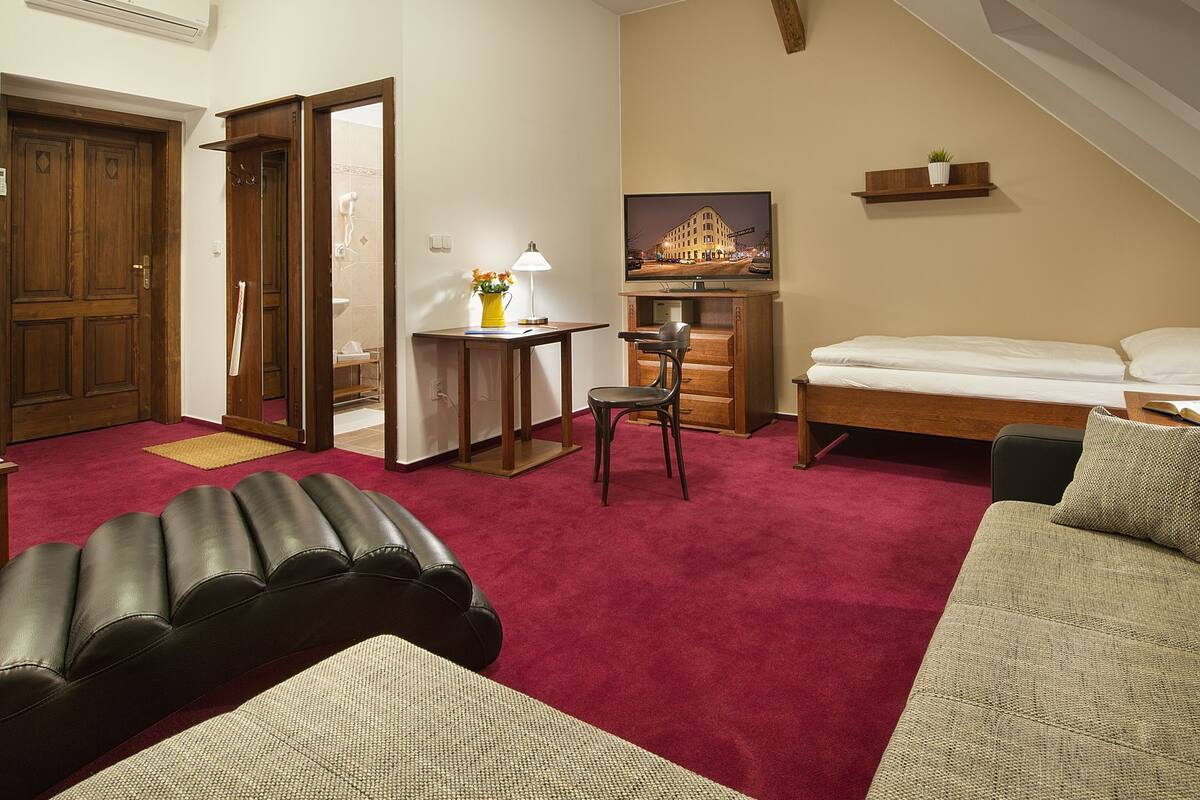 Une chambre d’hôtel avec un lit, un canapé, une chaise, une petite table avec une lampe, un miroir et un tableau au mur.