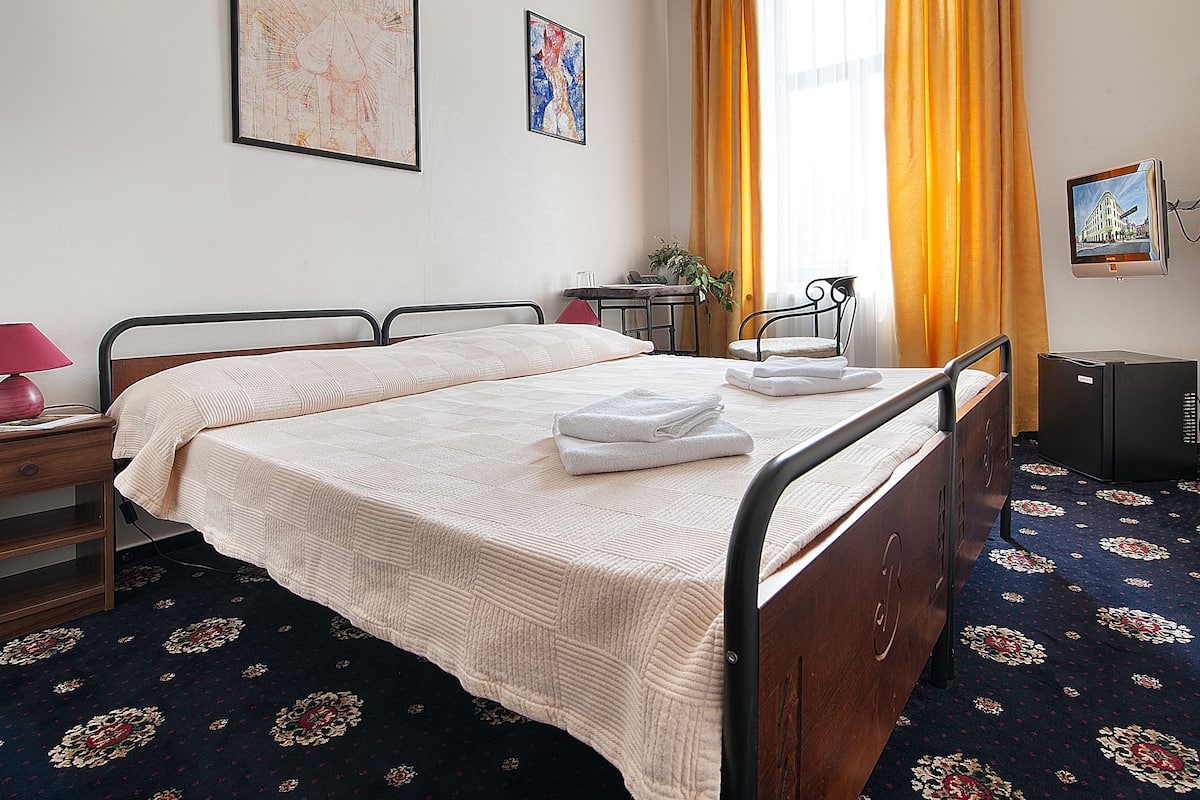 Un lit bien fait, avec une couette blanche, une table de chevet avec une lampe et une petite plante posée sur la table de chevet.