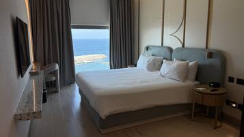 A hotel room with a large bed, a bedside table, a TV, and a view of the sea.