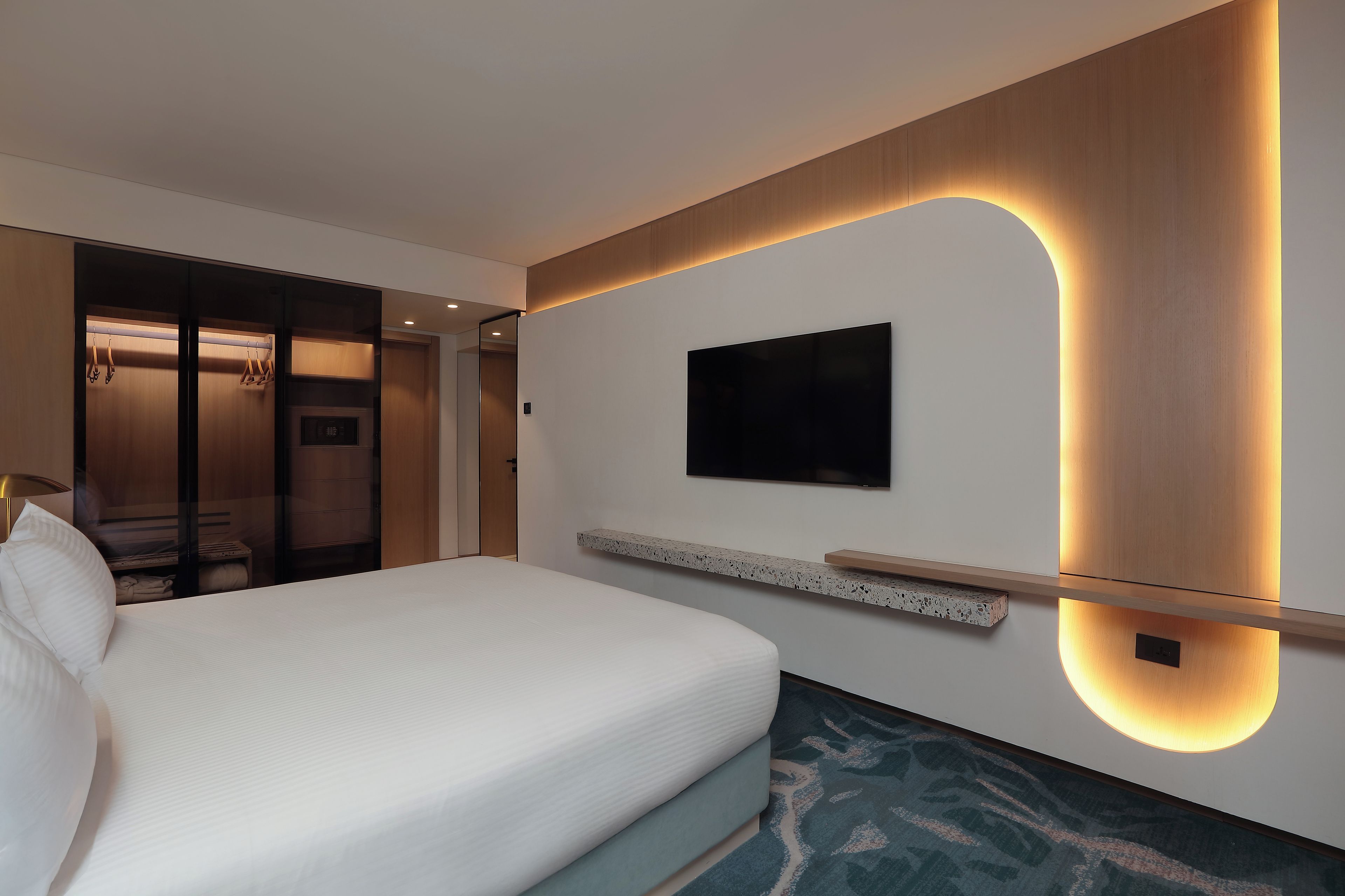 A modern hotel room with a large bed, a flat-screen TV mounted on the wall, and a built-in wardrobe.