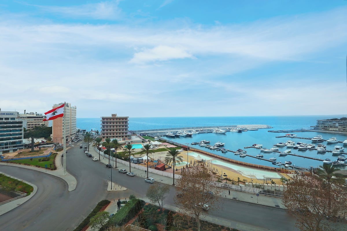 A marina with boats, a road, and buildings with a flag.