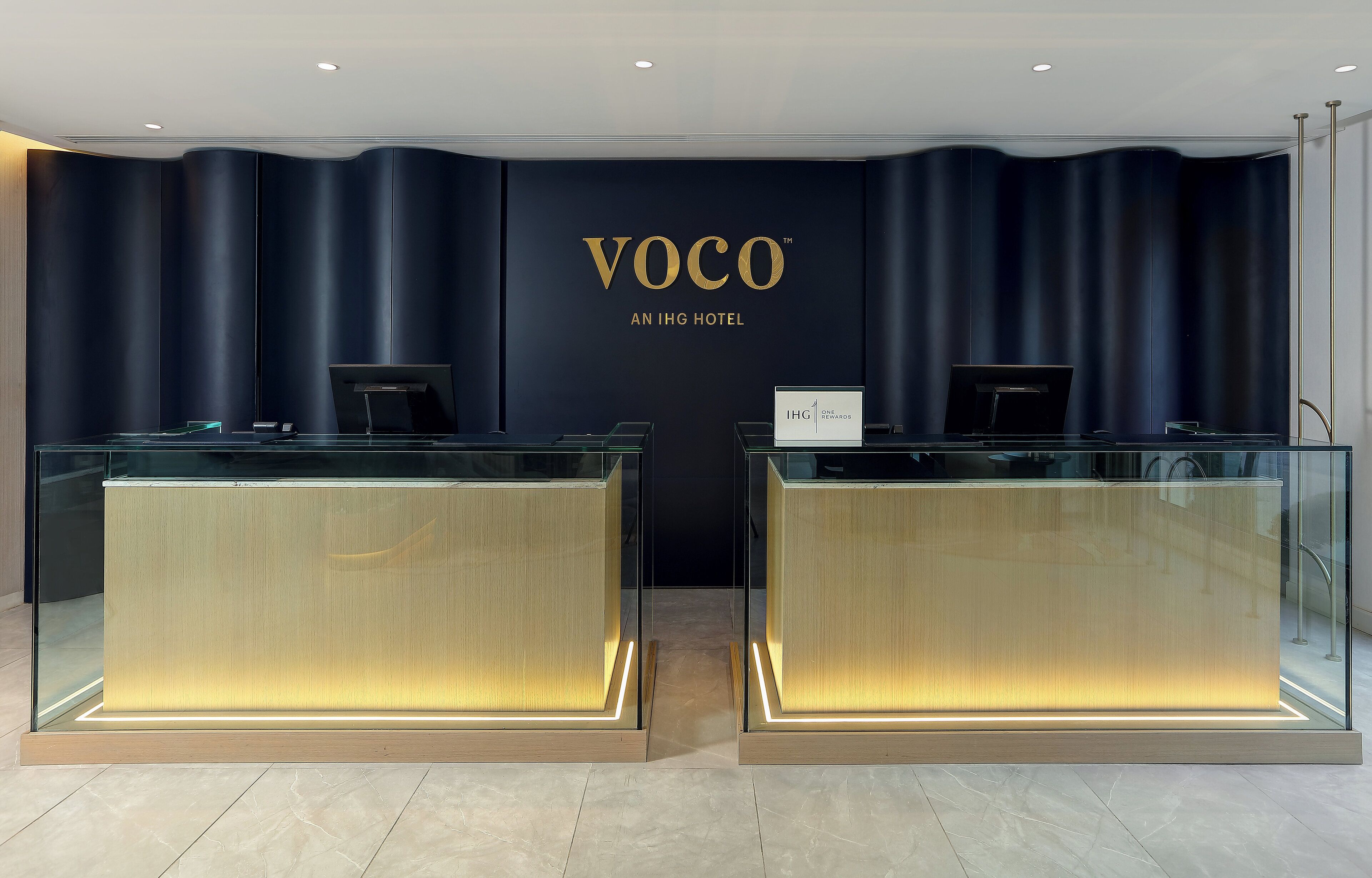 Un comptoir d’accueil avec un mur bleu foncé et l’inscription « VOCO, UN HÔTEL IHG ».