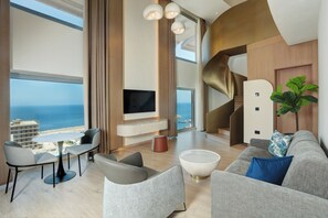 A modern living room with a large TV, seating, and a view of the sea. - voco Beirut Central District by IHG (Beirut)