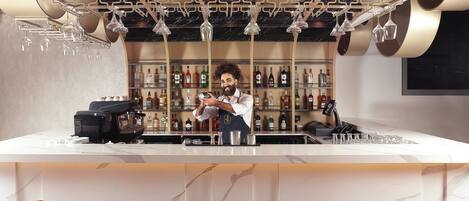 Zona de bar con un barista preparando bebidas, una máquina de café y una selección de botellas en estantes.