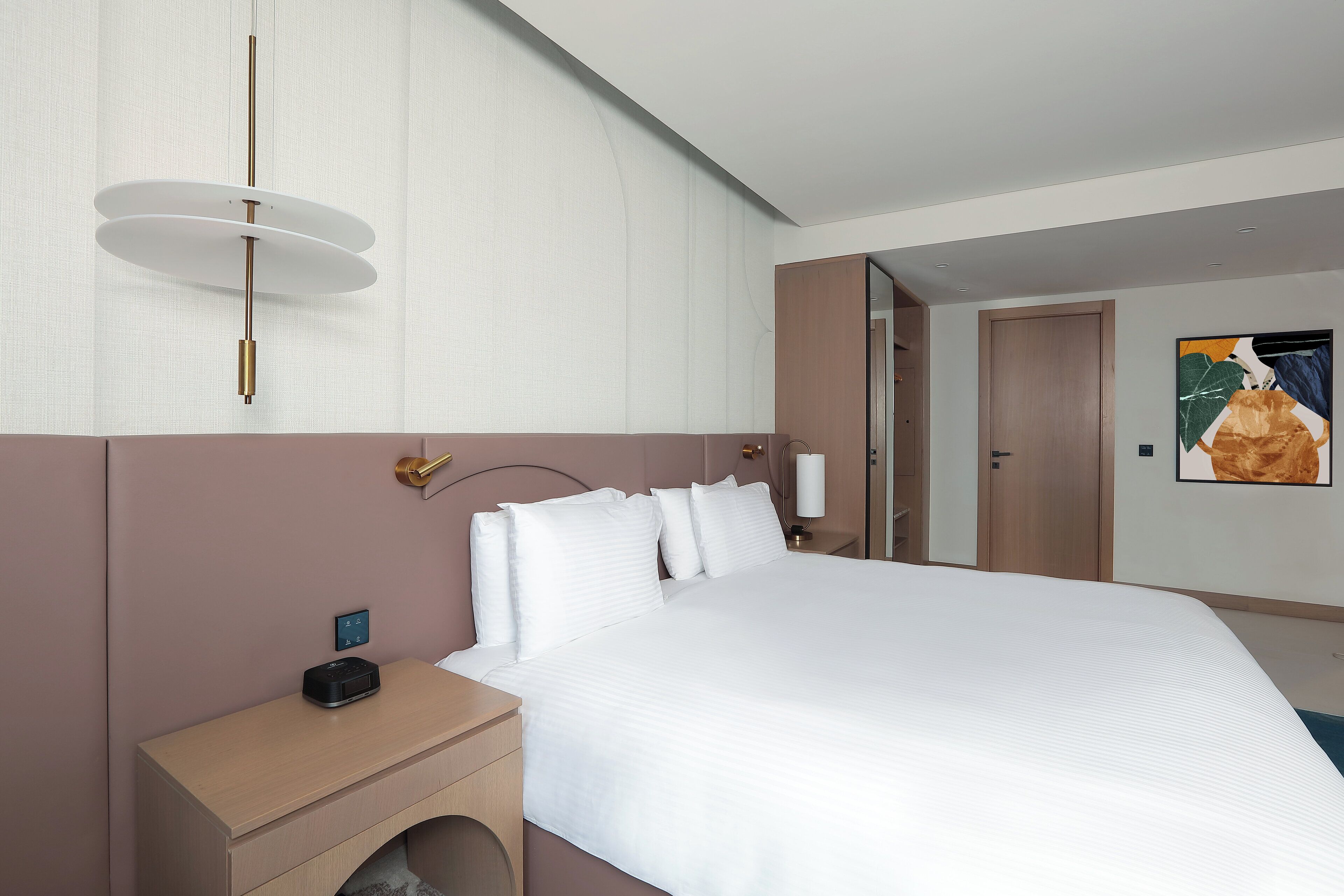A modern hotel room with a large bed, bedside tables, a wall-mounted light fixture, and a painting.