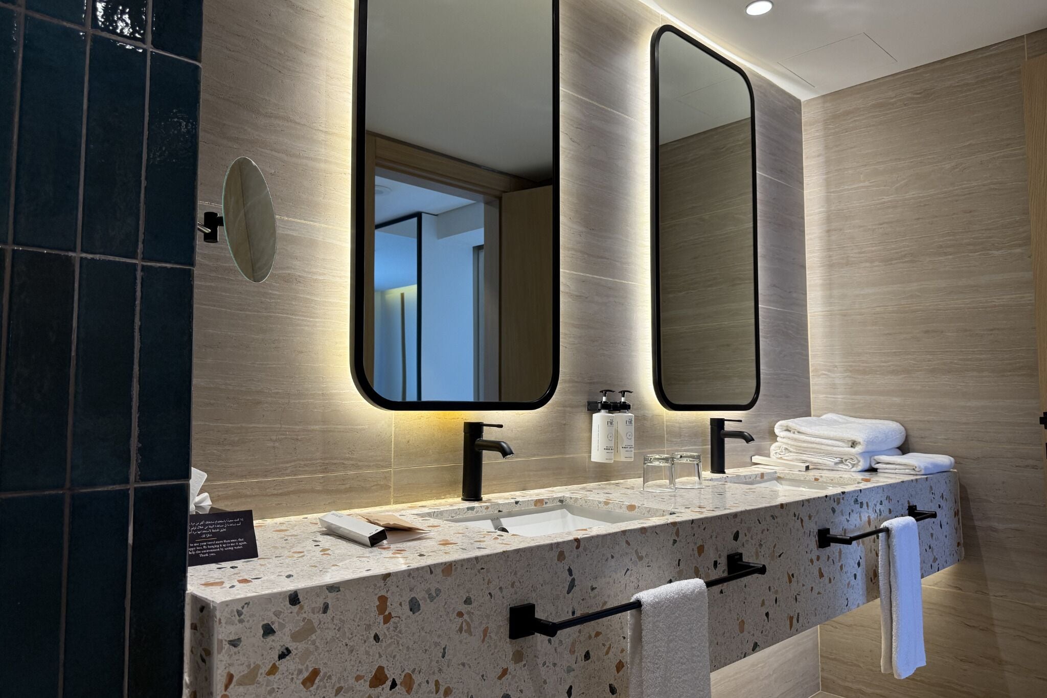 A modern bathroom with a granite countertop, two sinks, a large mirror, and a towel rack.