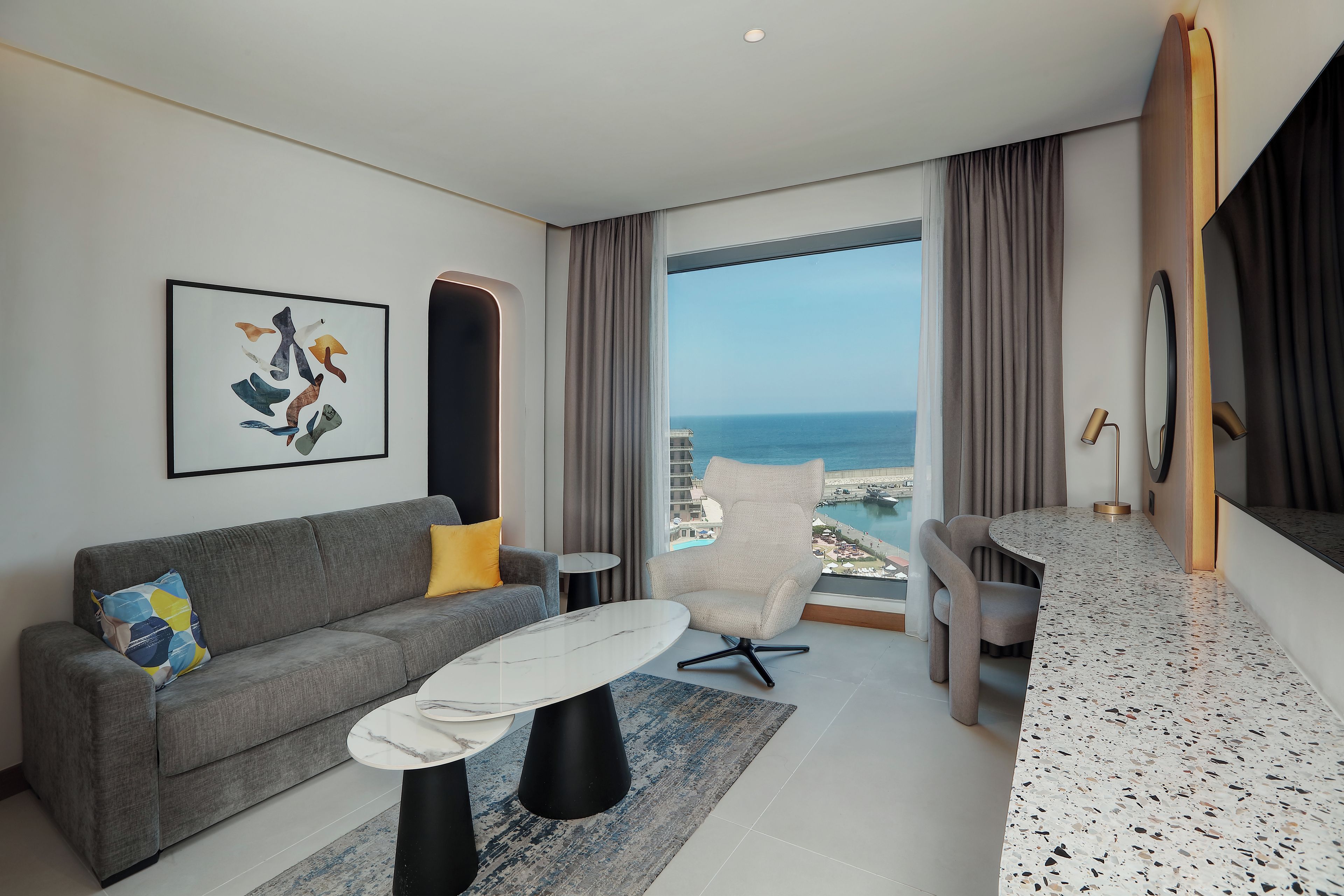A modern living room with a grey sofa, a marble coffee table, and a view of the sea.