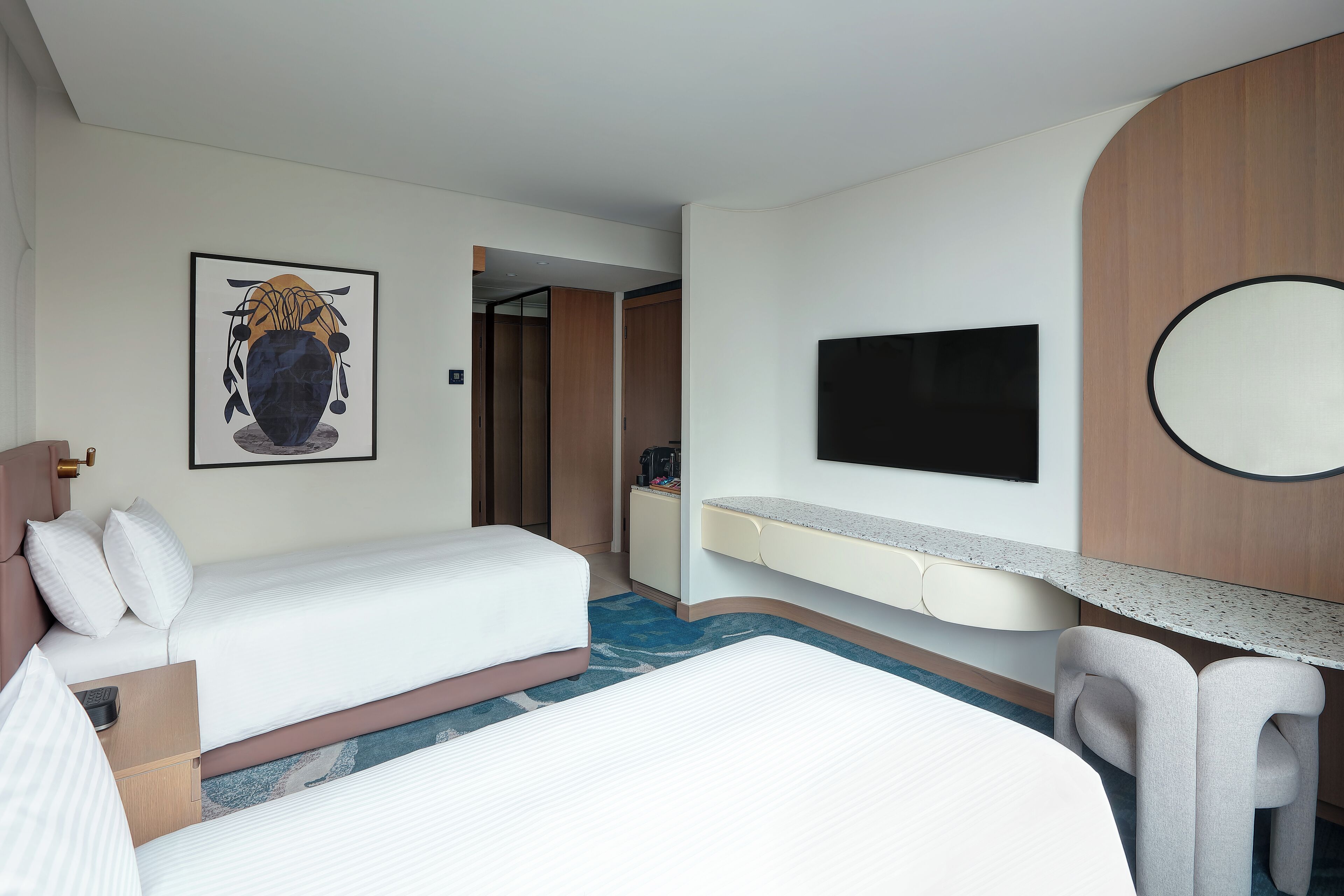 A hotel room with a bed, a desk, a TV, and a painting on the wall.
