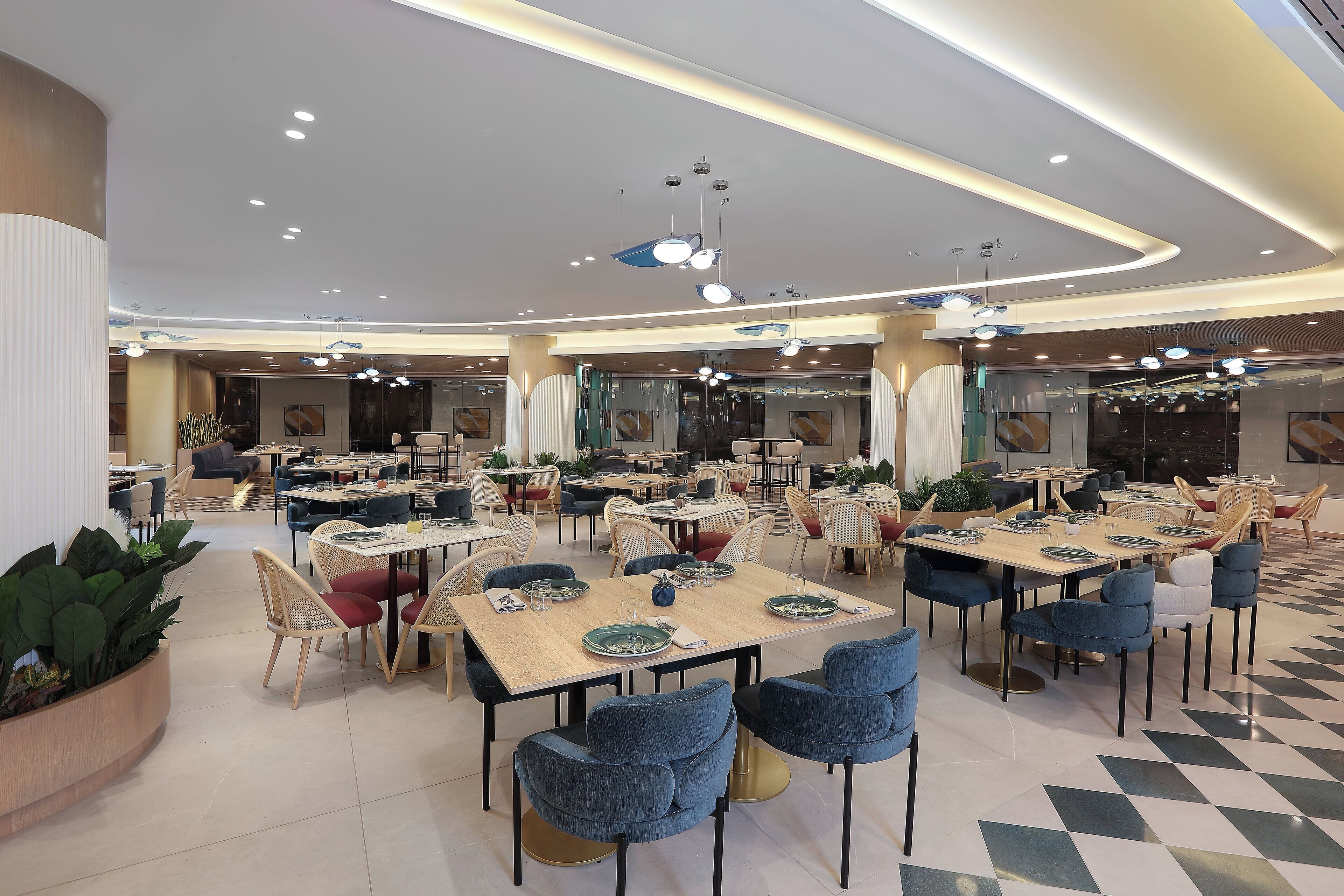 Un vaste espace dédié à la salle à manger, doté de nombreuses tables et chaises, et agrémenté d’un design de plafond moderne avec des luminaires encastrés et des suspensions.