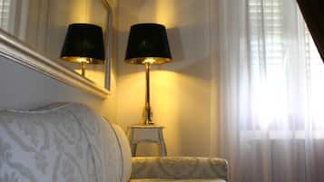A hotel room with a bed, two bedside lamps, a mirror, and a window with curtains.