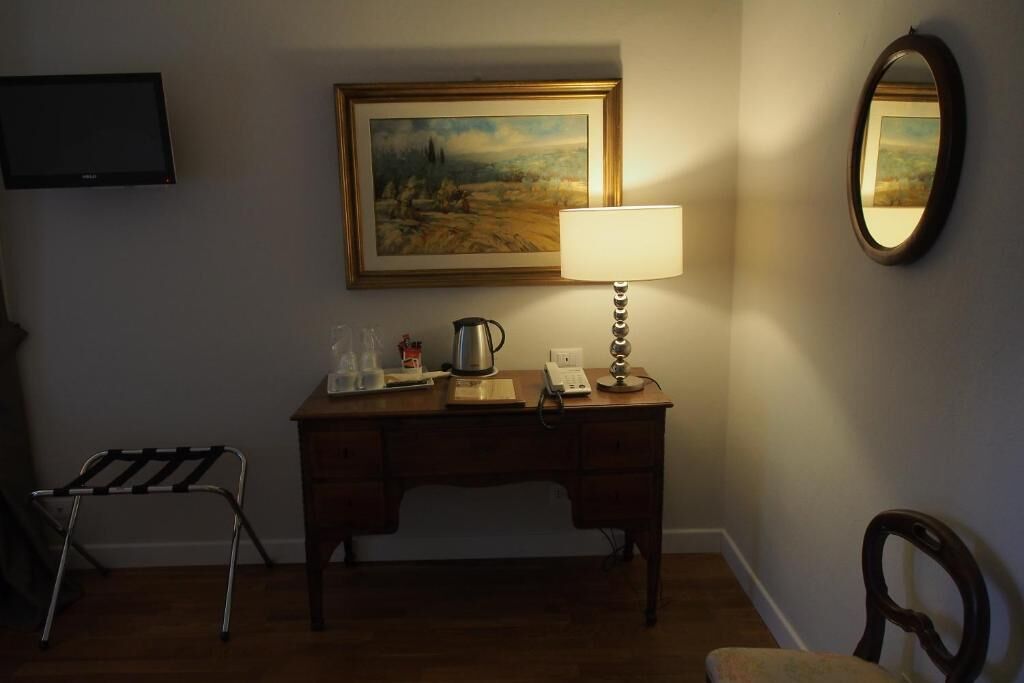 Una habitación con un escritorio de madera, una lámpara, un cuadro enmarco, un televisor y una silla.