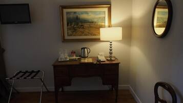 A room with a wooden desk, a lamp, a framed painting, a television, and a chair.