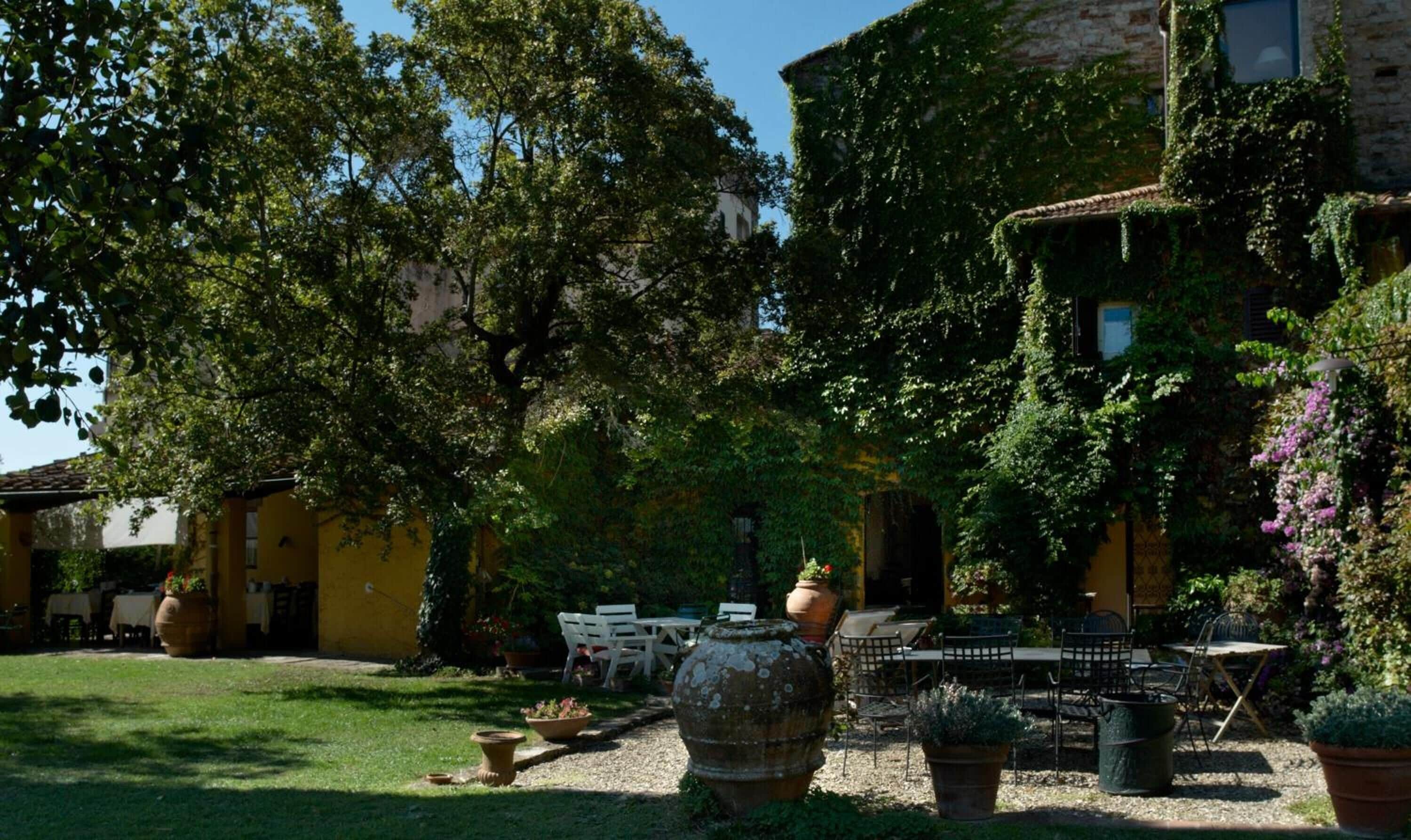 A courtyard with outdoor seating, surrounded by lush greenery and a yellow building.