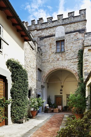 A courtyard with a stone building featuring an arched entrance, potted plants, and outdoor seating.