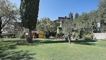 A courtyard with a stone wall, a large tree, and a building with a yellow facade.