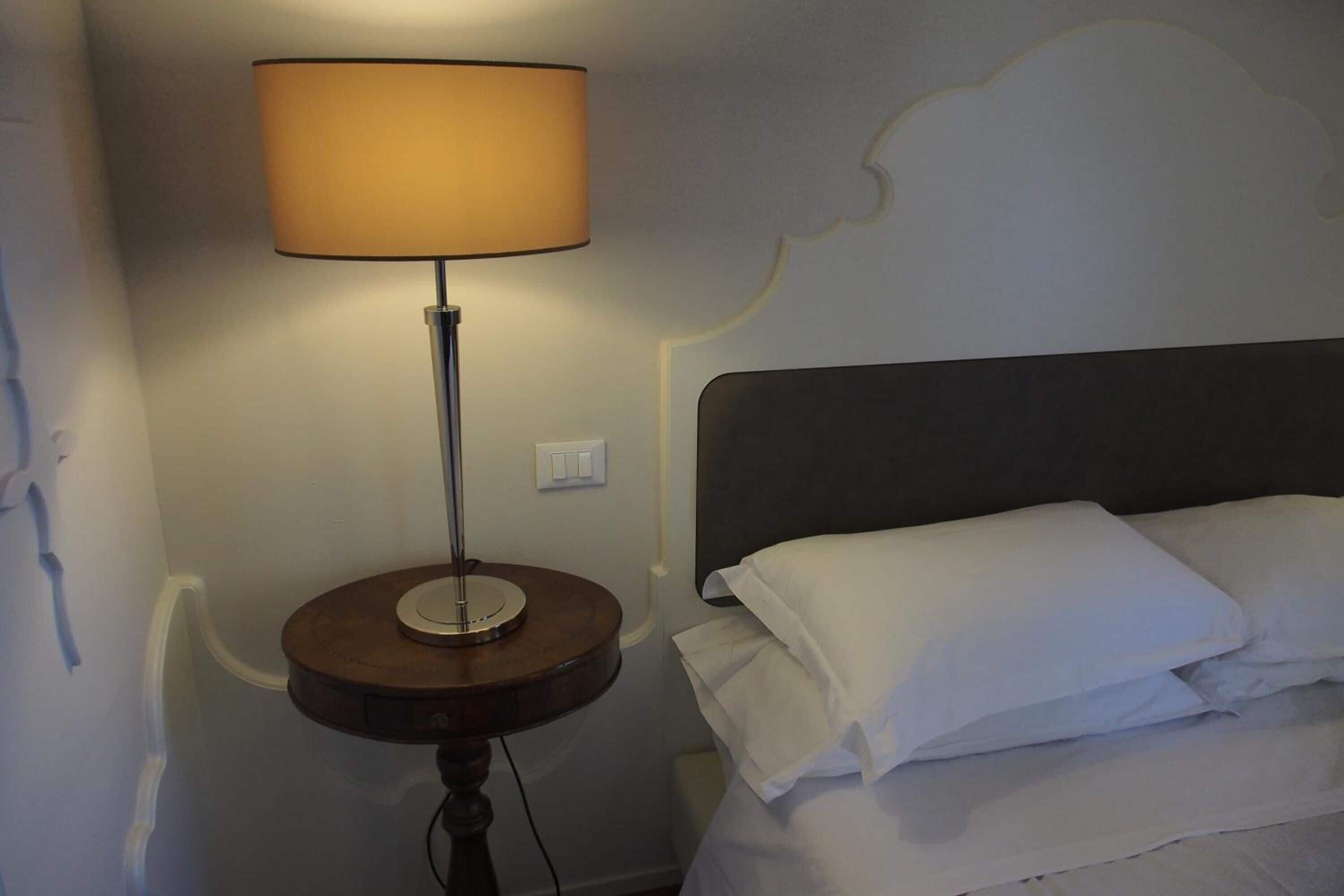 A bed with white linens and a round table with a lamp beside it.