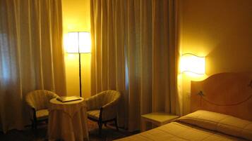 A hotel room with a bed, two chairs, a small table, and two lamps.