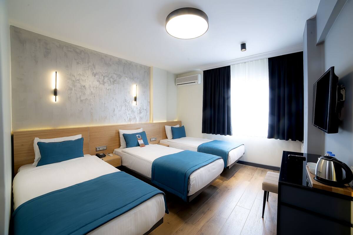 A hotel room with three beds, a flat-screen TV, a kettle, and a wooden desk.