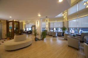 Un hall amplio con un sofá curvo, varios sillones y plantas en macetas.
