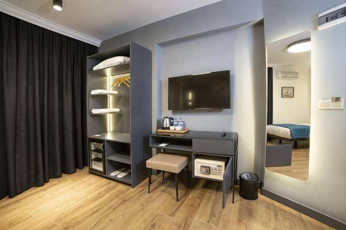 A hotel room with a desk, chair, TV, wardrobe, and a mirror.
