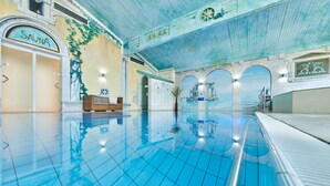 An indoor swimming pool with clear water, a sauna area, and a mural of a bridge and sea.