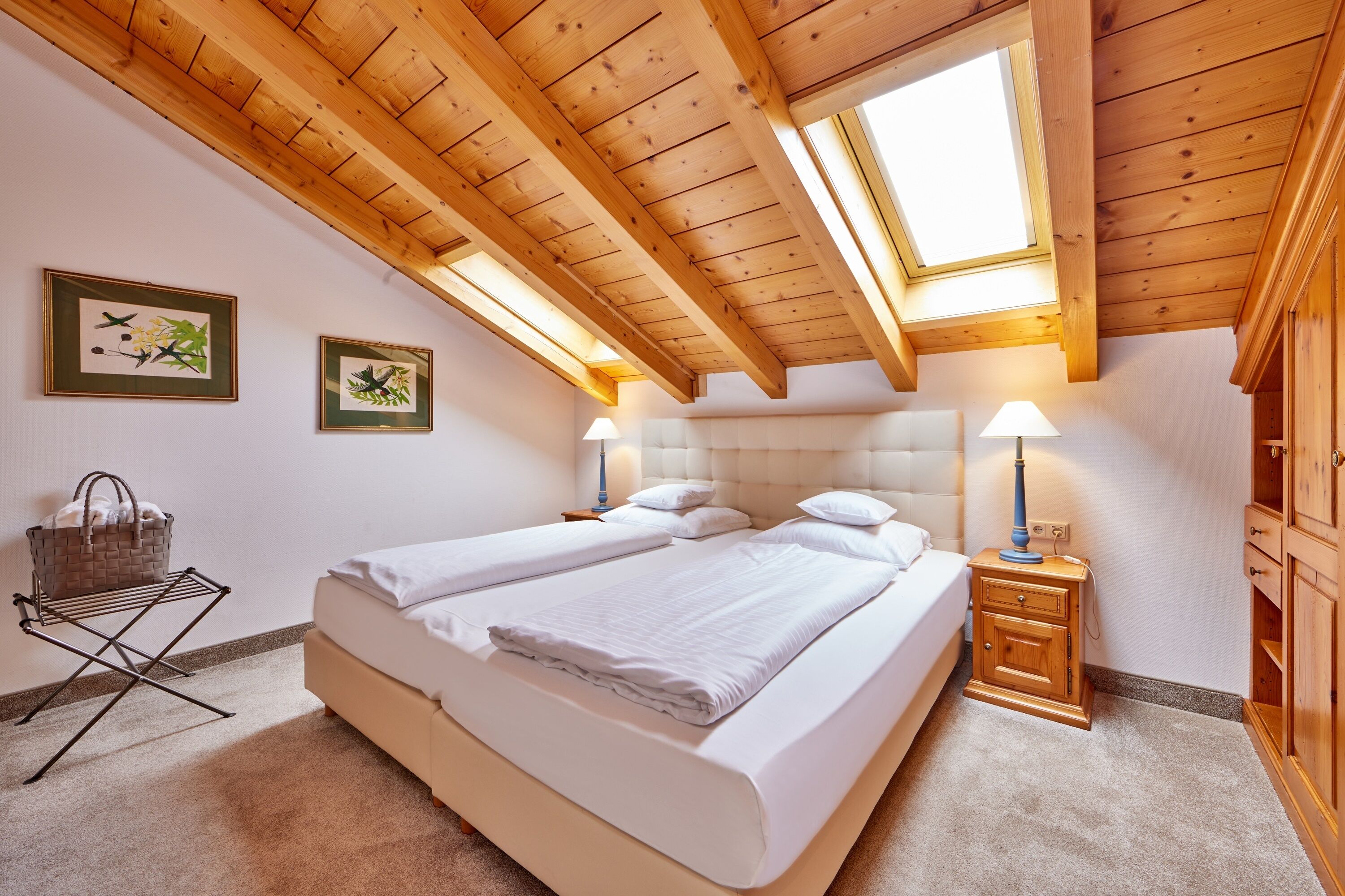 Un dormitorio con techo de madera, dos camas, una mesita de noche, una lámpara y una repisa en la pared.