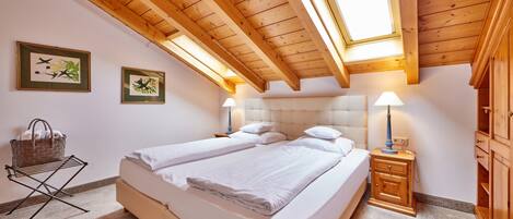 Un dormitorio con techo de madera, dos camas, una mesita de noche, una lámpara y una repisa en la pared.