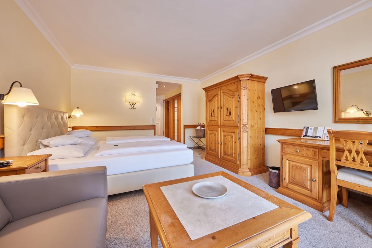 A hotel room with a bed, a wooden wardrobe, a television, and a desk with a chair.
