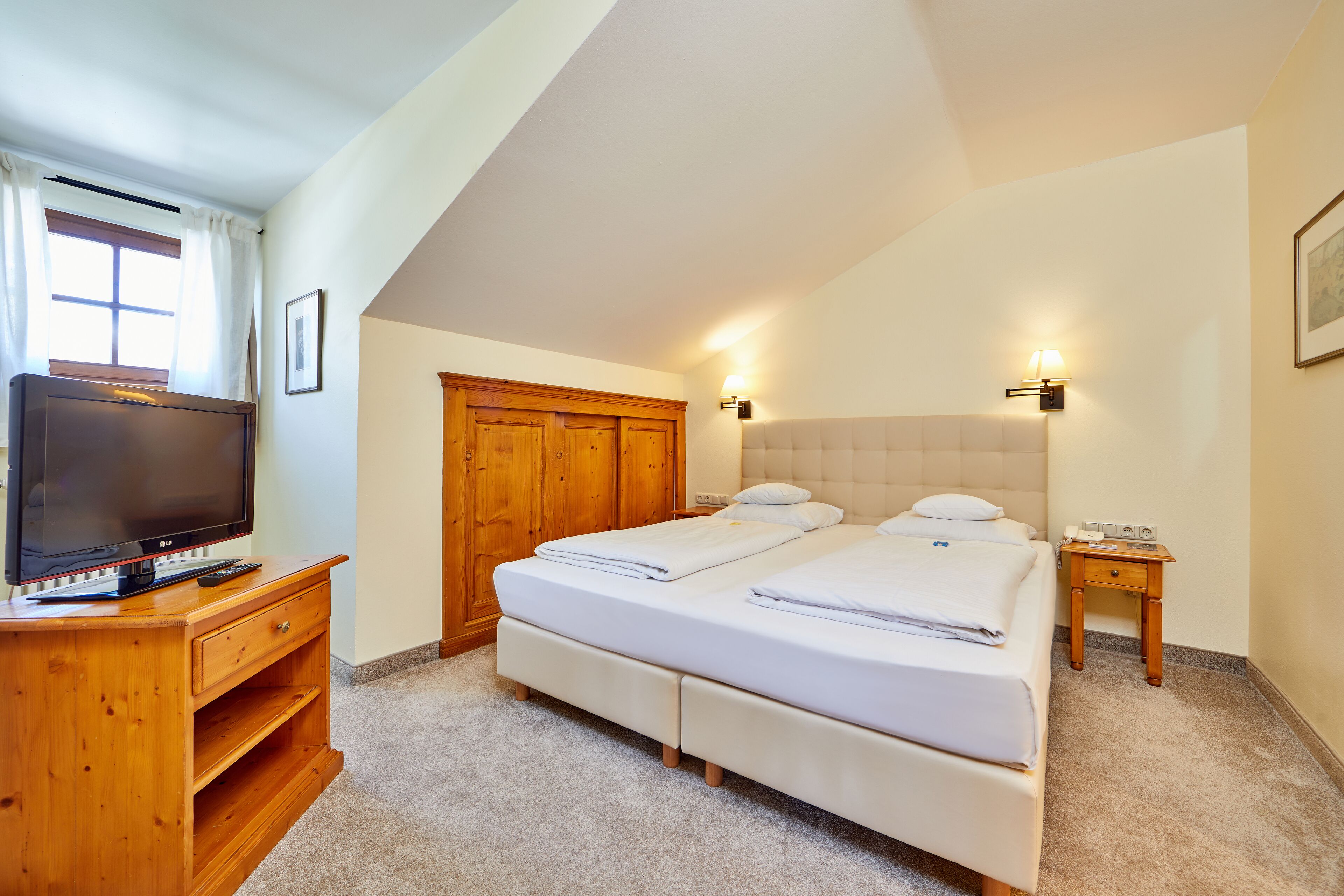 Quarto com duas camas, penteadeira de madeira, televisão e mesa de cabeceira.