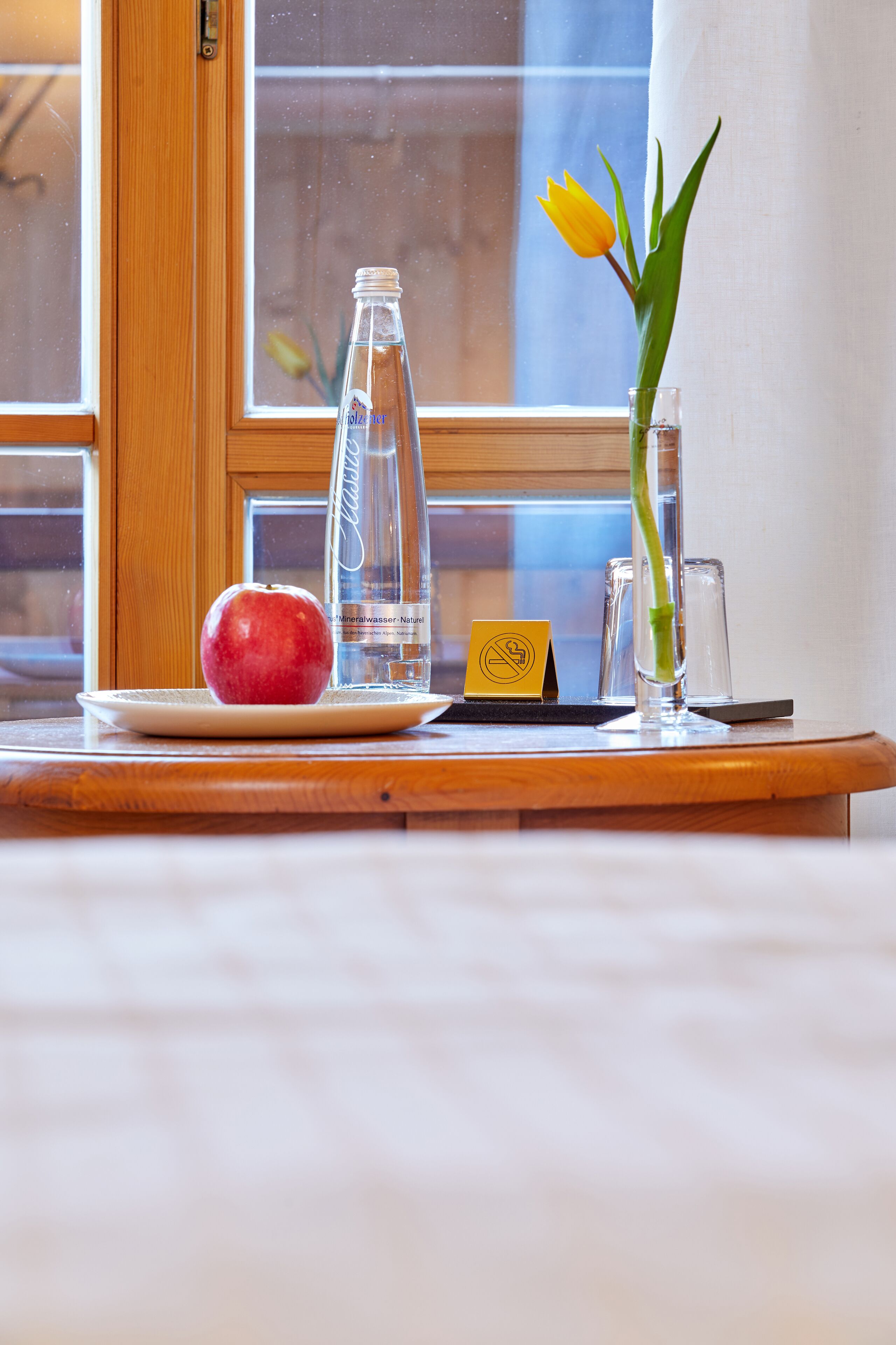 Een houten tafel met eten, een fles, een glas en een bloem.