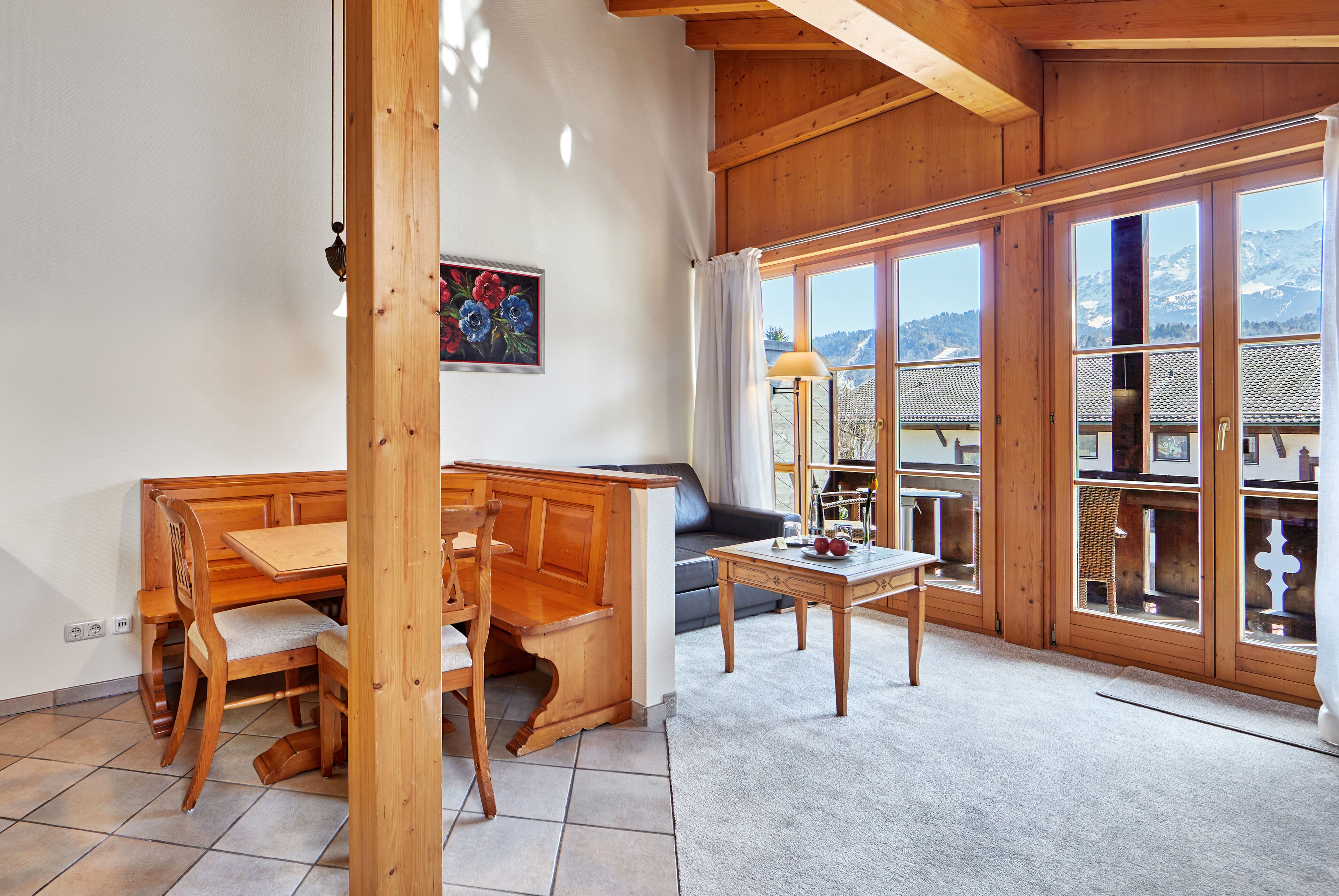 A wooden interior with a dining area, a sofa, and large windows offering a mountain view.