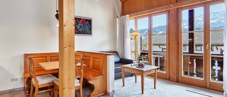 A wooden interior with a dining area, a sofa, and large windows offering a mountain view.
