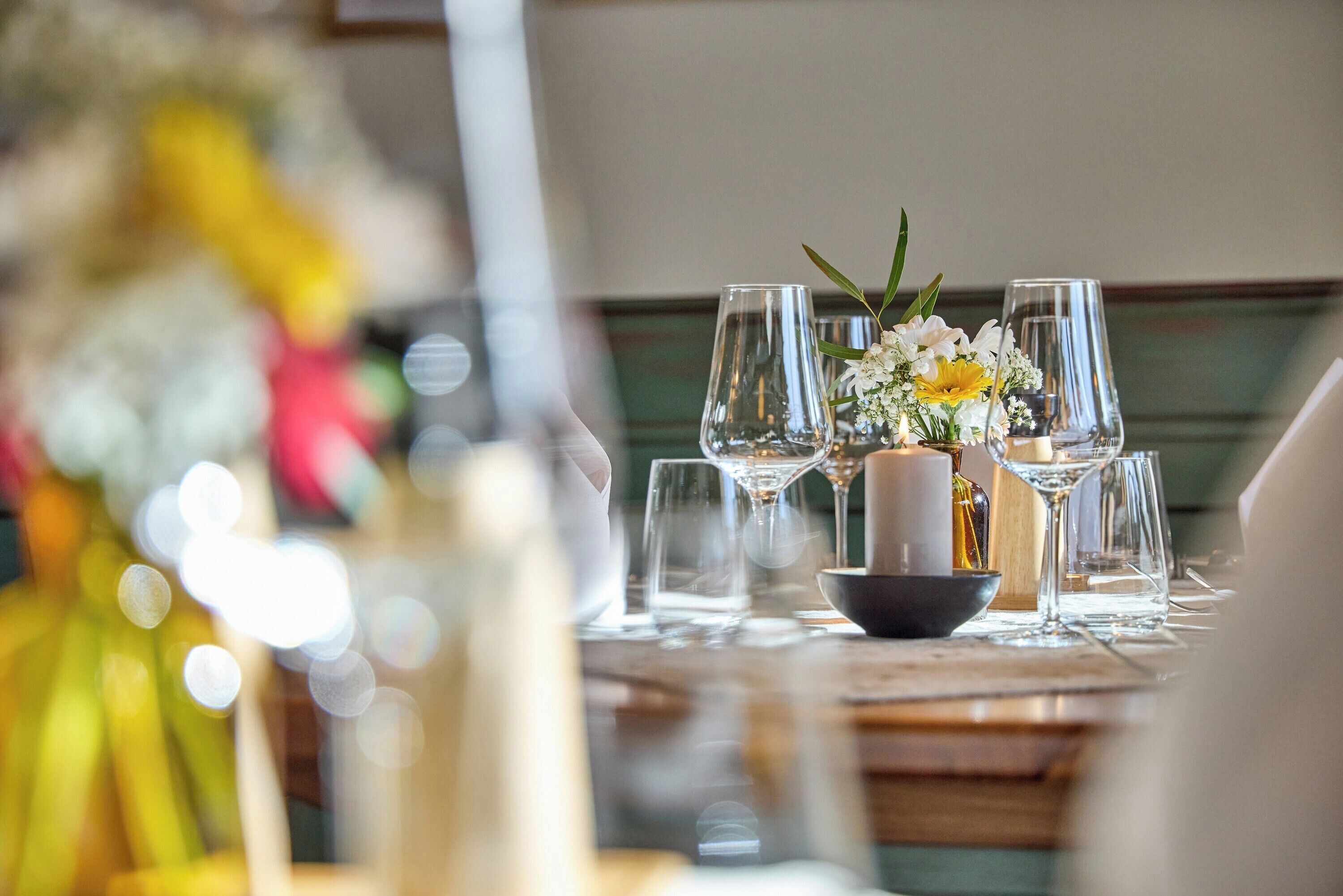 A dining table set with wine glasses, a bowl, and a centerpiece with flowers.