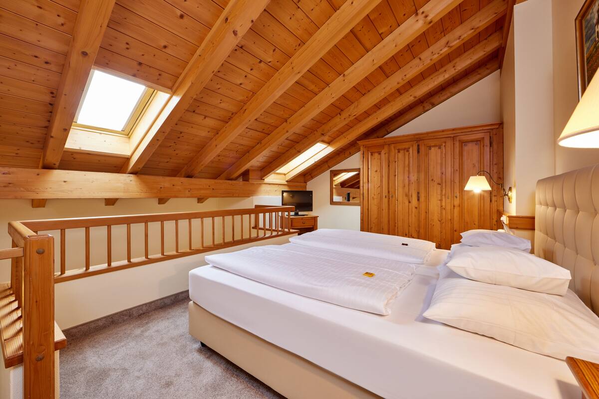 A bedroom with a wooden ceiling, a skylight, a bed with white linens, and wooden furniture.