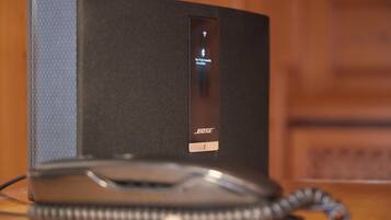 A black Bose speaker with a remote control and a coiled cord on a wooden surface.
