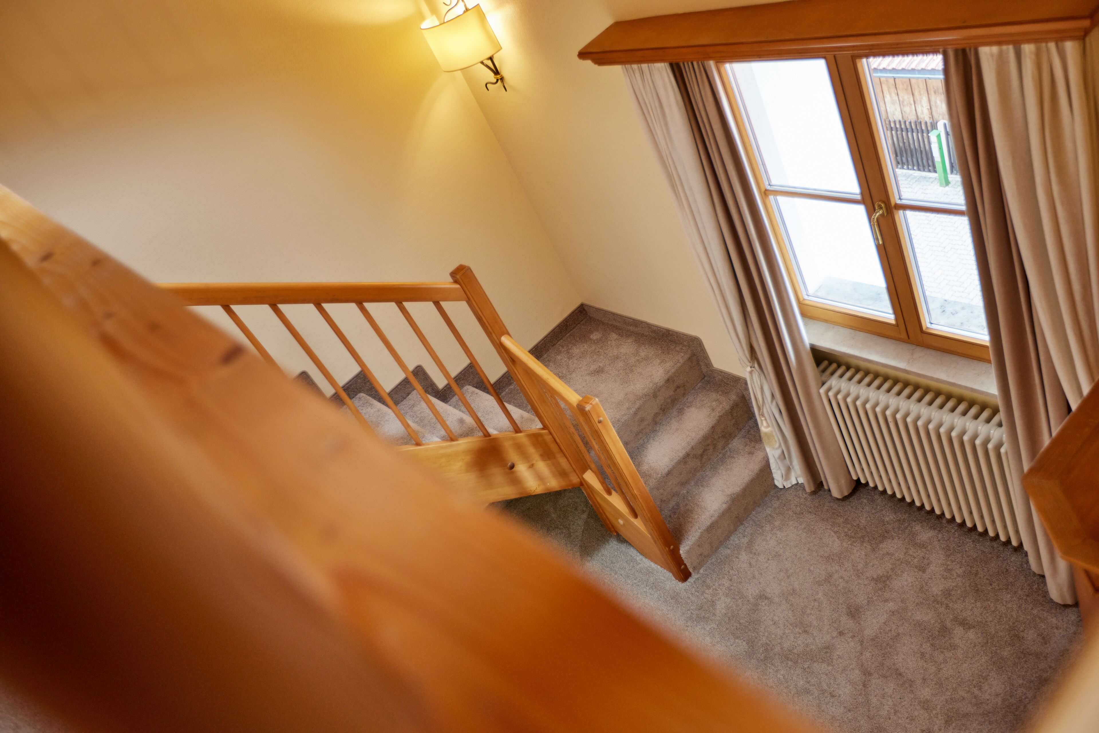 Una escalera de madera que lleva a una plataforma con un radiador y una ventana con cortinas.