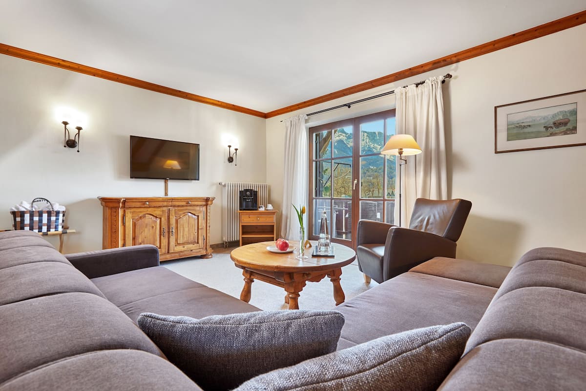 A living room with a large sofa, a wooden coffee table, a television, and a window with curtains.
