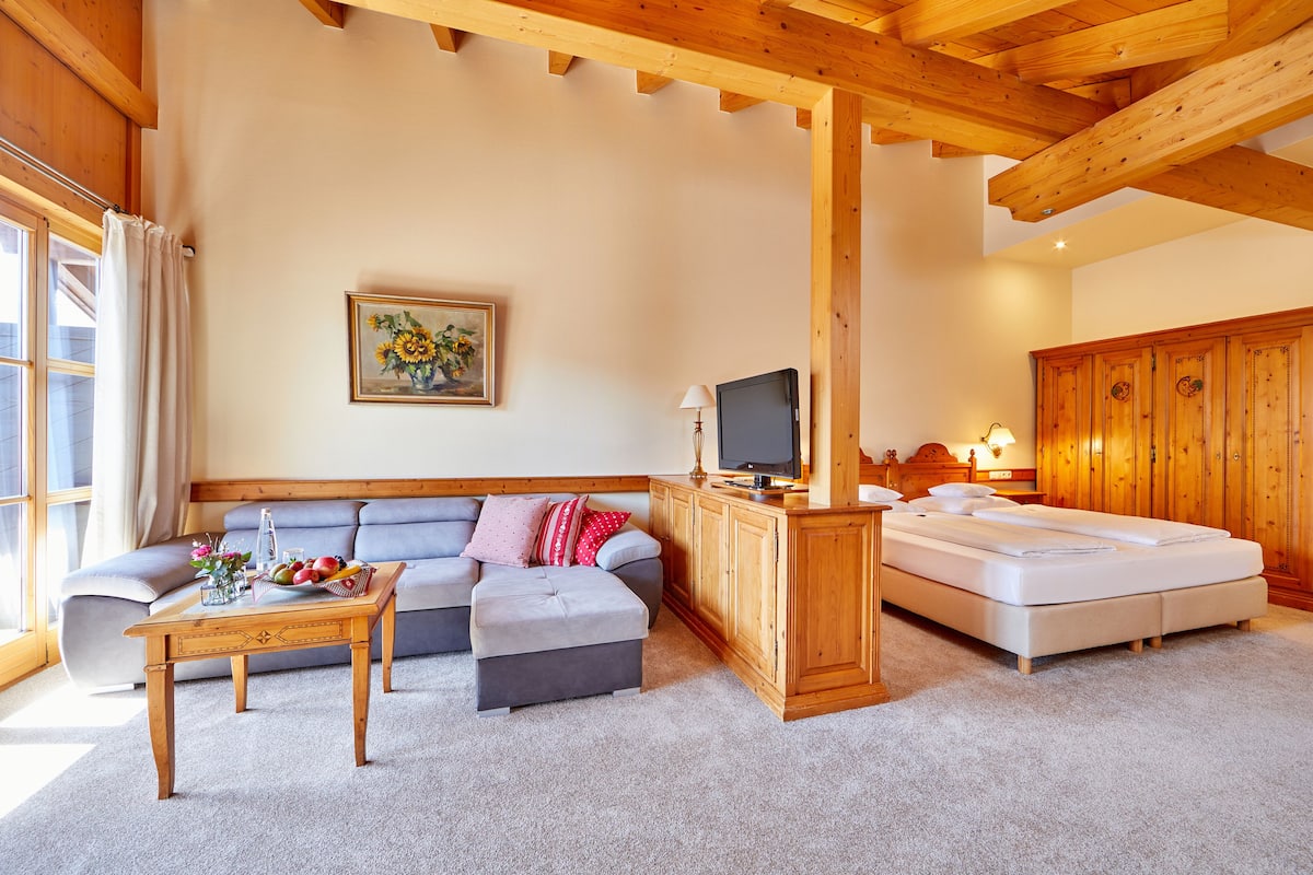 A cozy living room with a sofa, ottoman, wooden TV stand, and a bed.