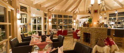 A cozy restaurant with wooden beams, red and white checkered tablecloths, and a stone fireplace.