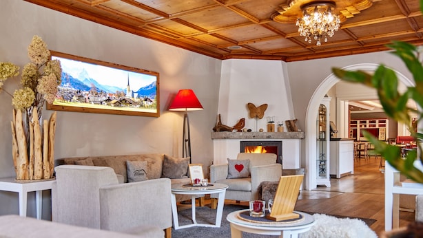 A cozy living room with a fireplace, comfortable seating, and a scenic view of a village through a large window.
