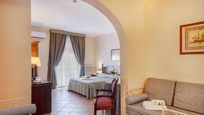 A hotel room with a bed, a sofa, a chair, and a small table with a lamp.