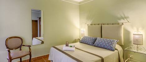 A hotel room with a bed, a chair, a nightstand, and a mirror.