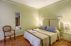 A hotel room with a bed, a chair, a nightstand, and a mirror.