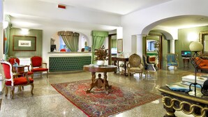 A hotel lobby with a reception desk, seating area, and a large decorative rug.
