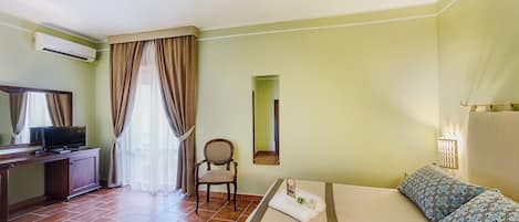 Habitación de hotel con cama, una silla, escritorio con televisor y ventana con cortinas.