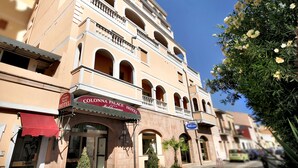 A hotel with a Mediterranean facade, multiple balconies, and a red awning.